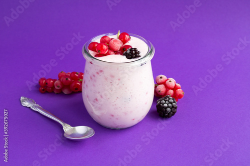 Fototapeta Closeup of milk yogurt with berries in the glass jar on the violet background