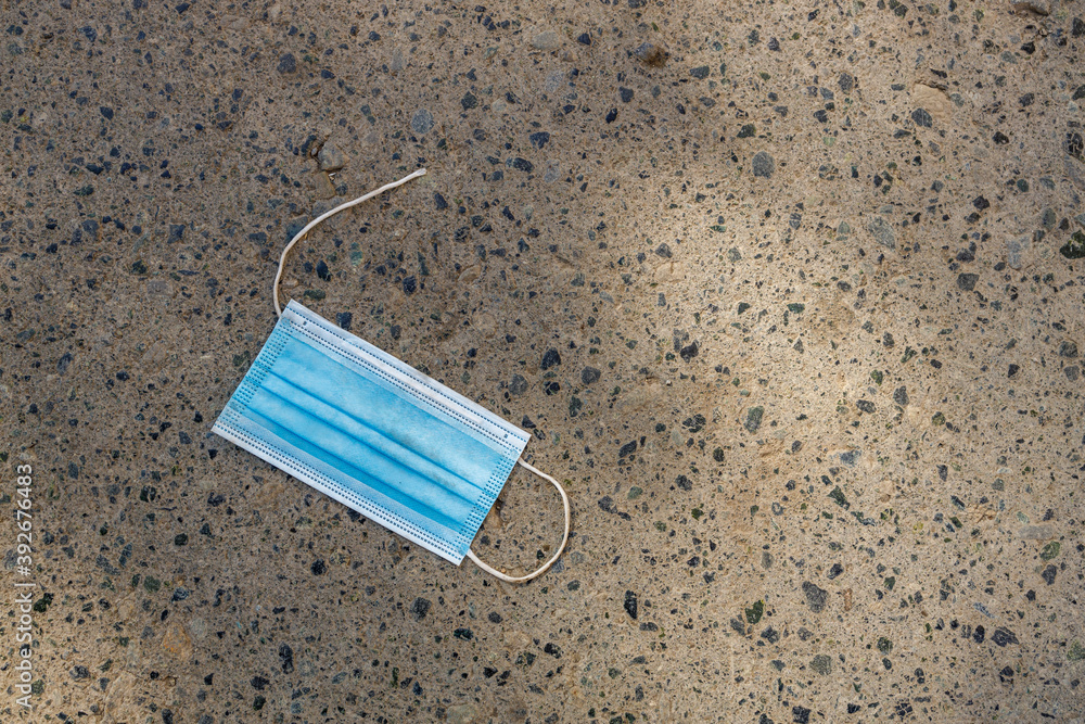 blue medical mask with a torn elastic band lies on the sidewalk blue medical mask with a torn elastic band lies on the sidewalk