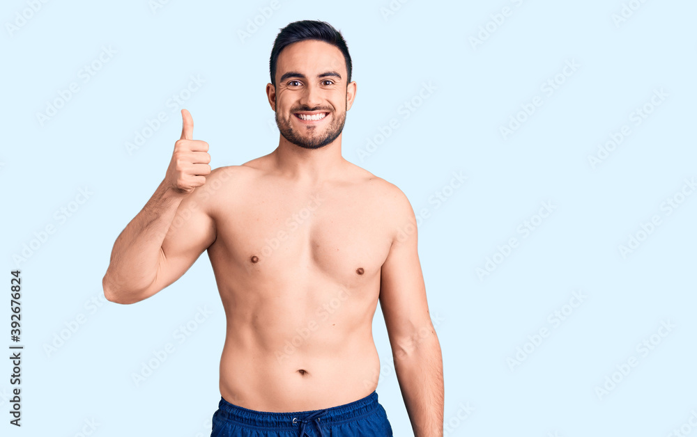 Young handsome man wearing swimwear smiling happy and positive, thumb up doing excellent and approval sign