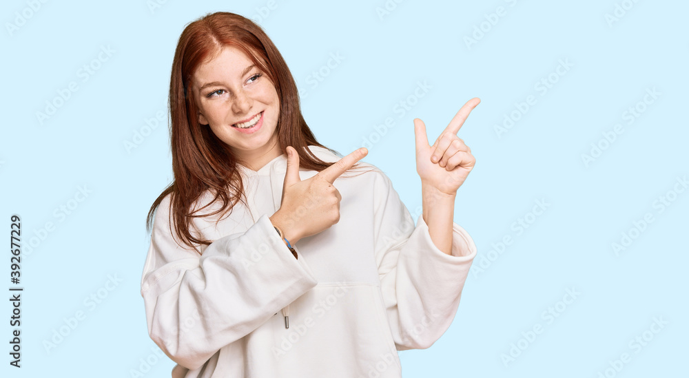 Young read head woman wearing casual sweatshirt smiling and looking at the camera pointing with two hands and fingers to the side. Young read head woman wearing casual sweatshirt smiling and looking at the camera pointing with two hands and fingers to the side.