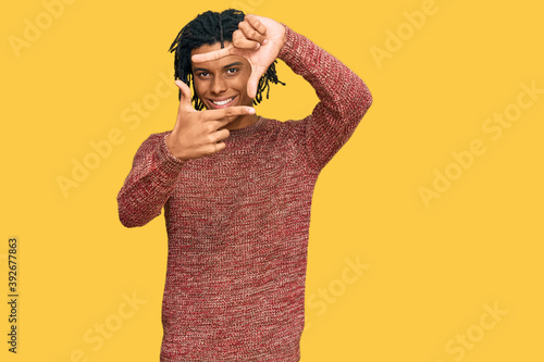 Young african american man wearing casual winter sweater smiling making frame with hands and fingers with happy face. creativity and photography concept.