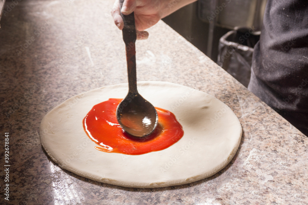 male chef smears tomato sauce on the base of the pizza. ketchup on pizza male chef smears tomato sauce on the base of the pizza. ketchup on pizza