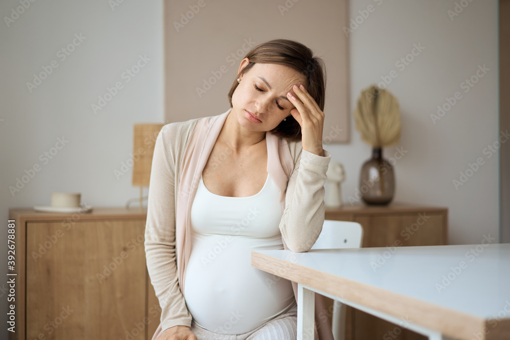 Pregnant woman suffering from headaches while sitting at the table. High quality photo Pregnant woman suffering from headaches while sitting at the table. High quality photo