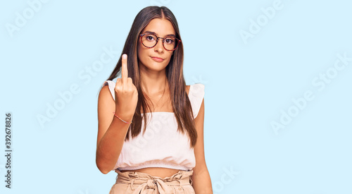 Young hispanic woman wearing casual clothes and glasses showing middle finger, impolite and rude fuck off expression
