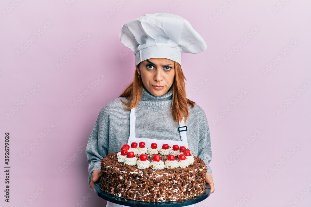 Hispanic young chef woman holding chocolate cake skeptic and nervous, frowning upset because of problem. negative person. Hispanic young chef woman holding chocolate cake skeptic and nervous, frowning upset because of problem. negative person.