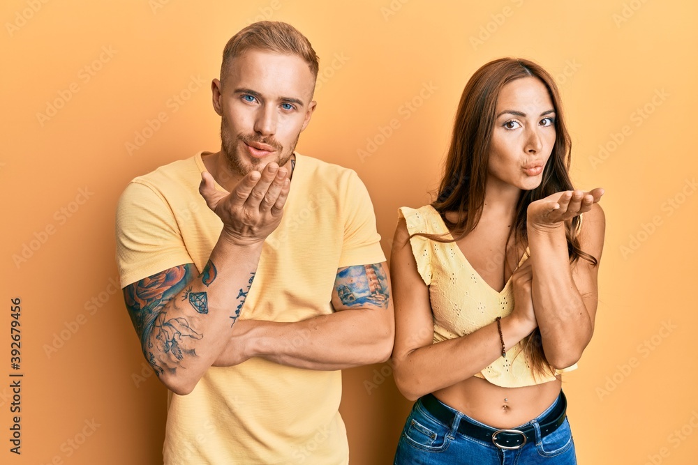 Young couple of girlfriend and boyfriend hugging and standing together looking at the camera blowing a kiss with hand on air being lovely and sexy. love expression.
