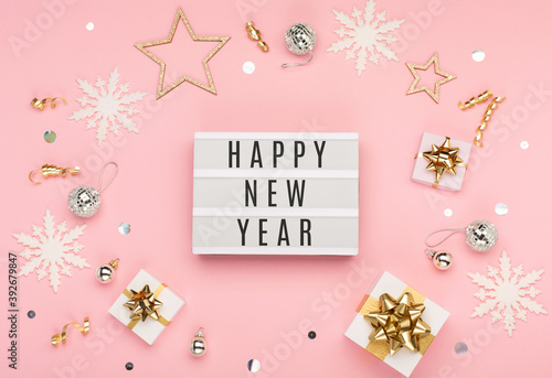 Happy New Year text on white Lightbox with gift boxes  holiday silver and gold decorations  snowflakes on pink paper background.