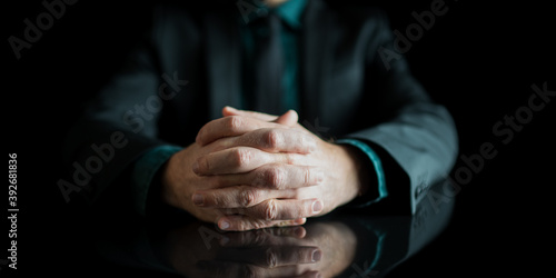 Businessman hands joined together resting on black desk with reflection