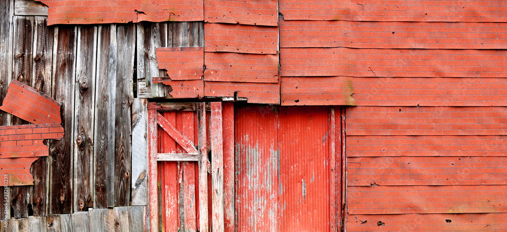 a very old deserted red neglected weathering empty abandoned historic farm barn building structure shed with deteriorating faded siding facade showing a exposed forsaken decay vintage exterior wall