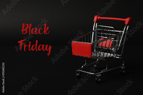 Phrase Black Friday and toy shopping cart on dark background