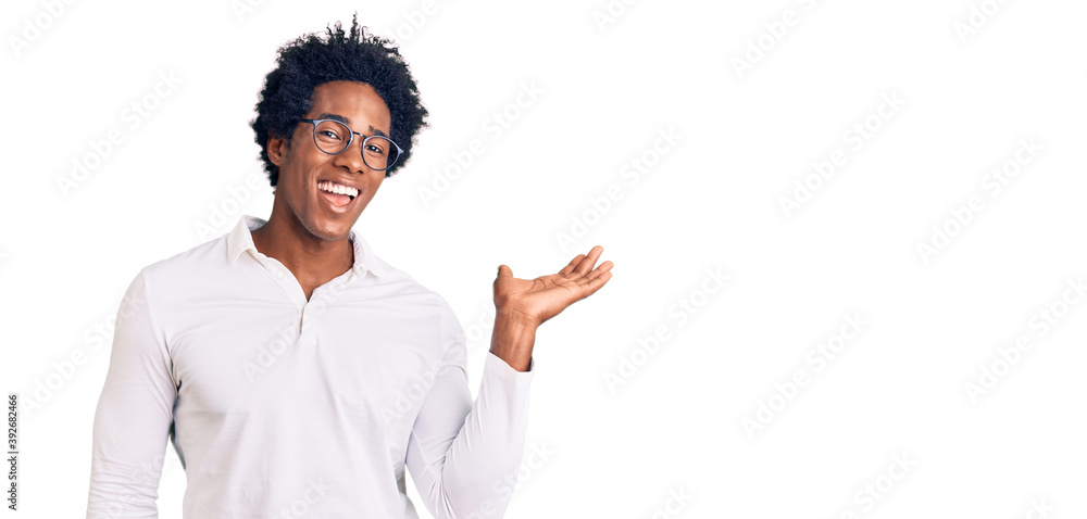 Handsome african american man with afro hair wearing casual clothes and glasses smiling cheerful presenting and pointing with palm of hand looking at the camera. Handsome african american man with afro hair wearing casual clothes and glasses smiling cheerful presenting and pointing with palm of hand looking at the camera.