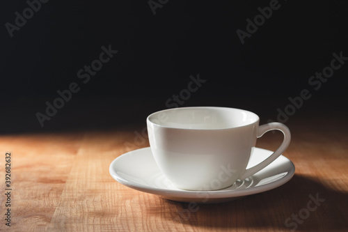 Empty white coffee cup or cappuccino mug on wooden table with dark background, copy-space