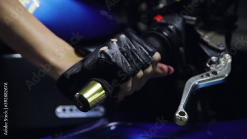 A woman's hand in a leather glove squeezes the clutch and turns the throttle grip of a sports motorcycle