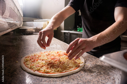 The chef sprinkles cheese on the pizza. Man prepares Italian pizza in the kitchen