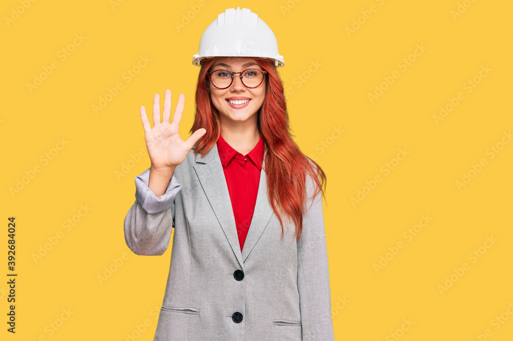 Young redhead woman wearing architect hardhat showing and pointing up with fingers number five while smiling confident and happy.