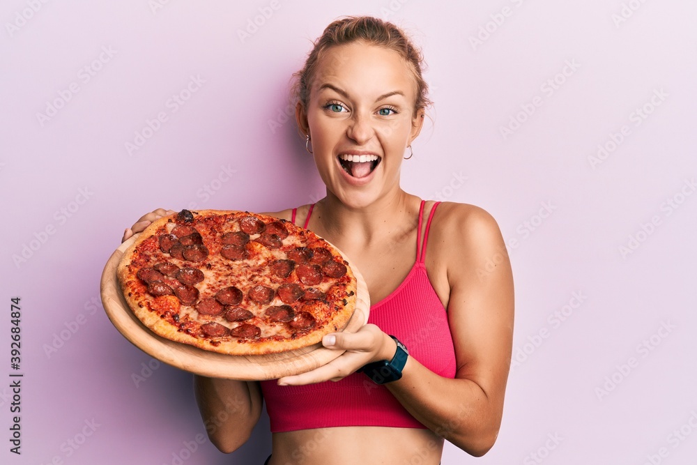 Beautiful caucasian woman holding italian pizza celebrating crazy and amazed for success with open eyes screaming excited. Beautiful caucasian woman holding italian pizza celebrating crazy and amazed for success with open eyes screaming excited.