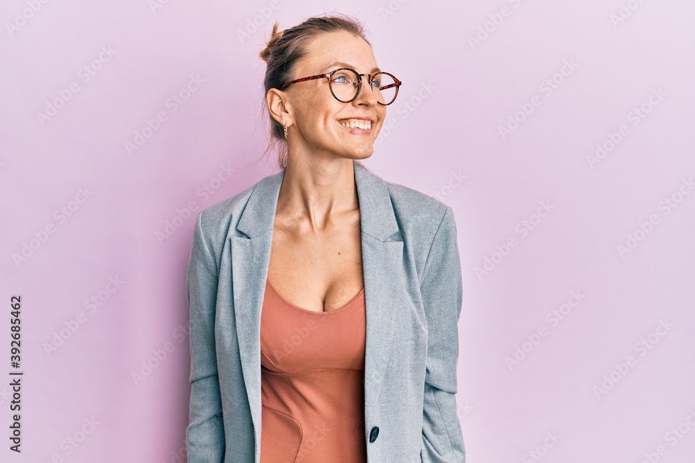 Beautiful caucasian woman wearing business jacket and glasses looking away to side with smile on face, natural expression. laughing confident.