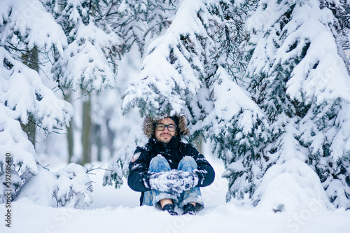 Cute adult man sitting under snowy firs