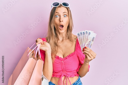 Beautiful caucasian woman holding shopping bags and 500 russian ruble afraid and shocked with surprise and amazed expression, fear and excited face.