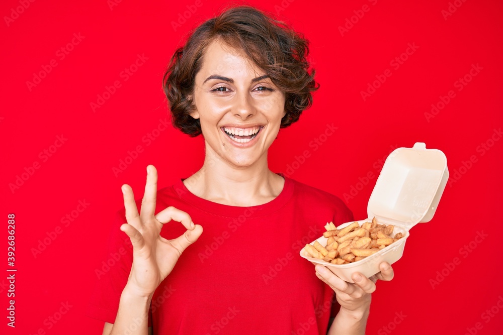 Young hispanic woman holding potato chip doing ok sign with fingers, smiling friendly gesturing excellent symbol Young hispanic woman holding potato chip doing ok sign with fingers, smiling friendly gesturing excellent symbol