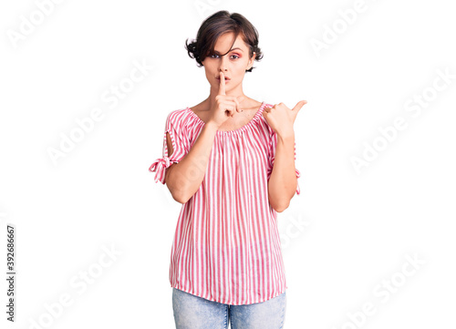 Beautiful young woman with short hair wearing casual summer clothes asking to be quiet with finger on lips pointing with hand to the side. silence and secret concept.
