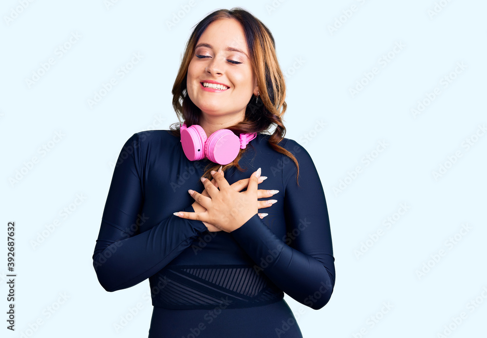 Young beautiful caucasian woman wearing gym clothes and using headphones smiling with hands on chest with closed eyes and grateful gesture on face. health concept. Young beautiful caucasian woman wearing gym clothes and using headphones smiling with hands on chest with closed eyes and grateful gesture on face. health concept.