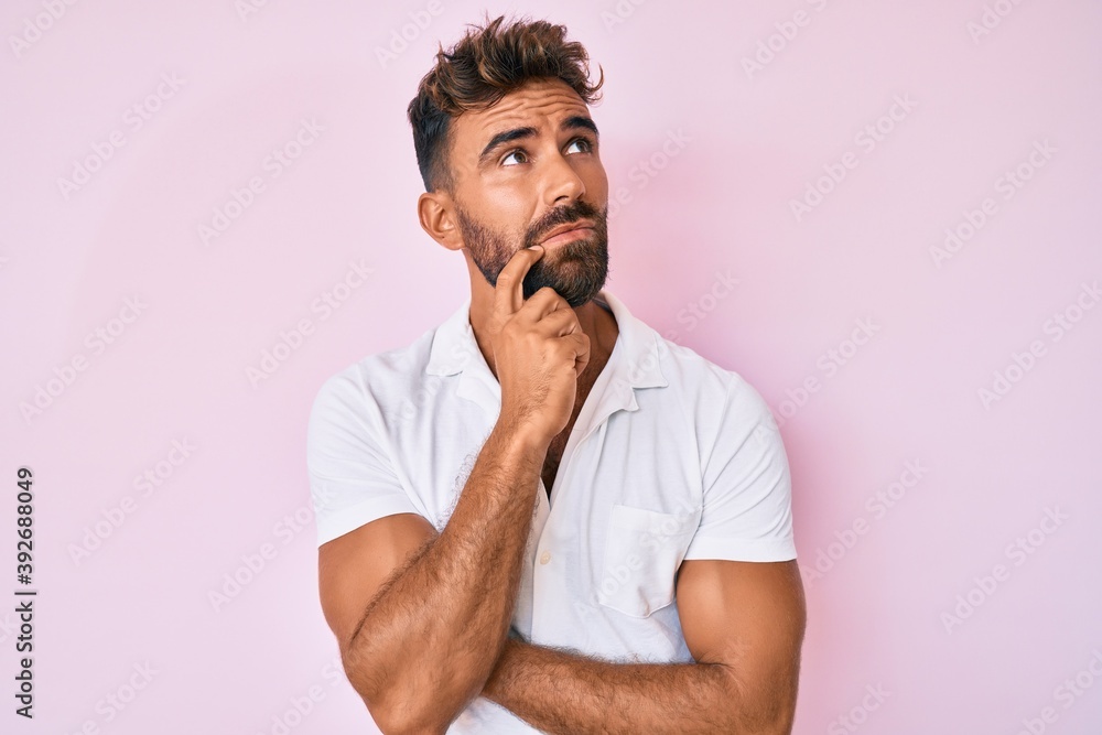 Young hispanic man wearing casual clothes serious face thinking about question with hand on chin, thoughtful about confusing idea Young hispanic man wearing casual clothes serious face thinking about question with hand on chin, thoughtful about confusing idea