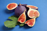 Delicious ripe figs with green leaf on blue background, closeup