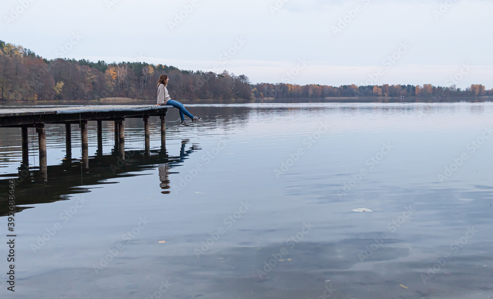 Attractive young female sitting at the edge of a pier while enjoying the views of a lake in Trakai, Lithuania. This city was the ancient capital of this baltic republic.