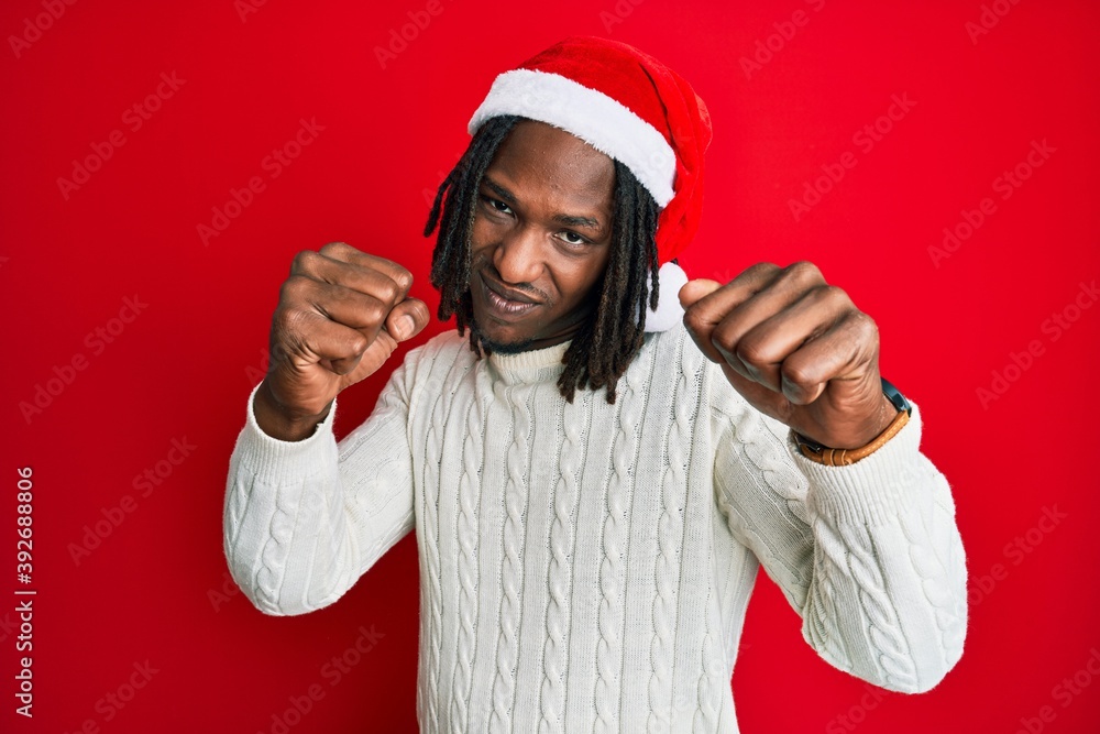 African american man with braids wearing christmas hat punching fist to fight, aggressive and angry attack, threat and violence African american man with braids wearing christmas hat punching fist to fight, aggressive and angry attack, threat and violence