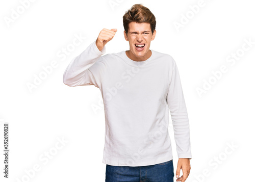 Handsome caucasian man wearing casual white sweater angry and mad raising fist frustrated and furious while shouting with anger. rage and aggressive concept.