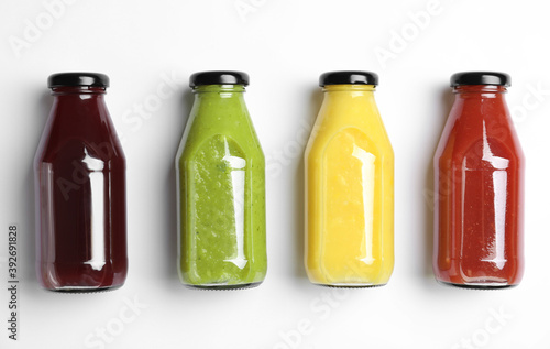 Bottles with delicious colorful juices on white background, flat lay