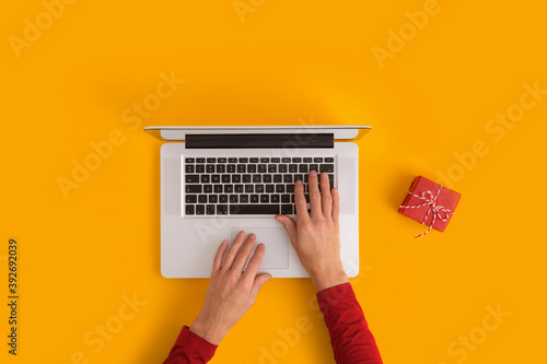 Man working on laptop and red gift on the table. Top view.