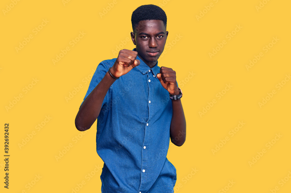 Young african american man wearing casual clothes punching fist to fight, aggressive and angry attack, threat and violence Young african american man wearing casual clothes punching fist to fight, aggressive and angry attack, threat and violence