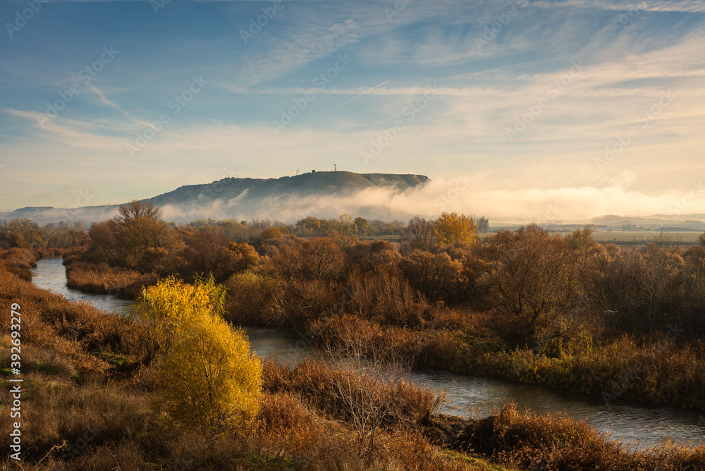 Beautiful landscape of the river bank with the autumn colors in the trees and the mist covering the mountain, Torrejón de Ardoz, Madrid, Spain Beautiful landscape of the river bank with the autumn colors in the trees and the mist covering the mountain, Torrejón de Ardoz, Madrid, Spain