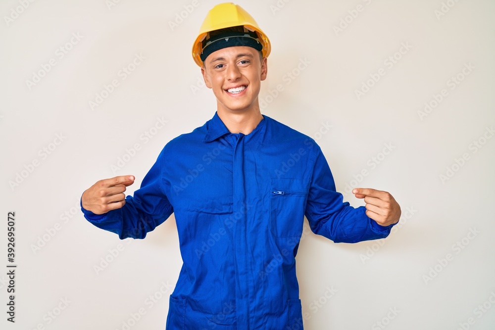 Young hispanic boy wearing worker uniform and hardhat looking confident with smile on face, pointing oneself with fingers proud and happy.