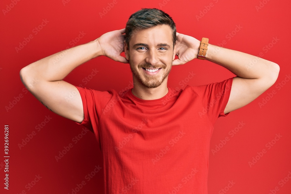 Handsome caucasian man wearing casual red tshirt relaxing and stretching, arms and hands behind head and neck smiling happy Handsome caucasian man wearing casual red tshirt relaxing and stretching, arms and hands behind head and neck smiling happy