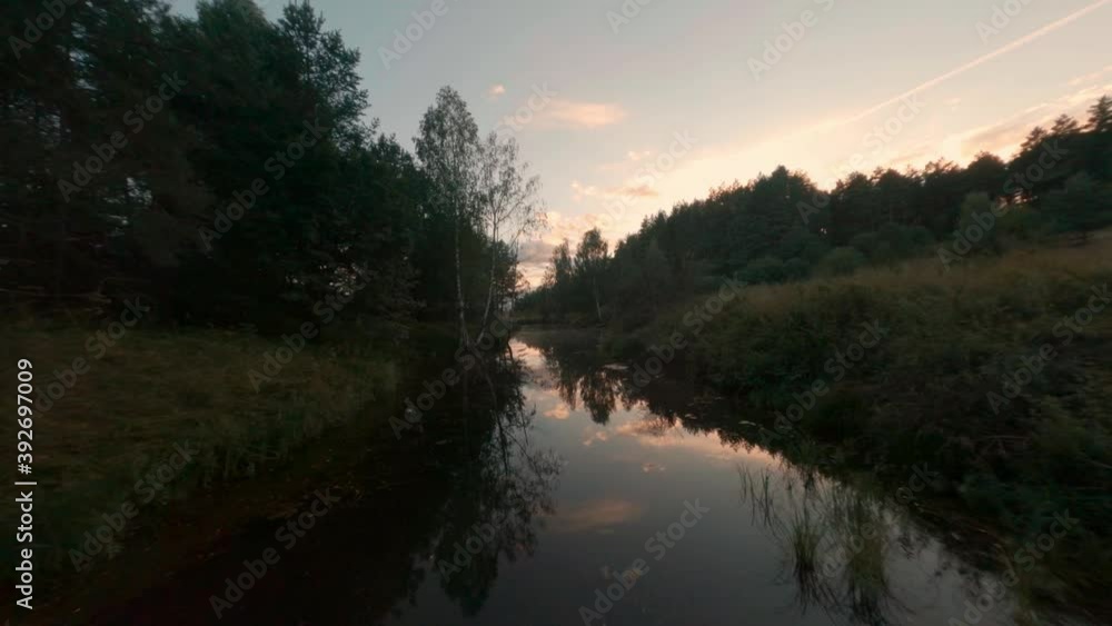 Fpv sport drone flying over calm river surface and clear sky reflecting in water like mirror. Summer stream flowing on green forest landscape. Evening nature in summer village cinematic drone above. Fpv sport drone flying over calm river surface and clear sky reflecting in water like mirror. Summer stream flowing on green forest landscape. Evening nature in summer village cinematic drone above.