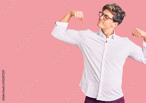 Young handsome man wearing business clothes and glasses showing arms muscles smiling proud. fitness concept.
