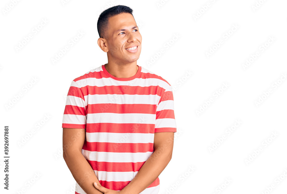 Young handsome latin man wearing casual clothes looking away to side with smile on face, natural expression. laughing confident. Young handsome latin man wearing casual clothes looking away to side with smile on face, natural expression. laughing confident.