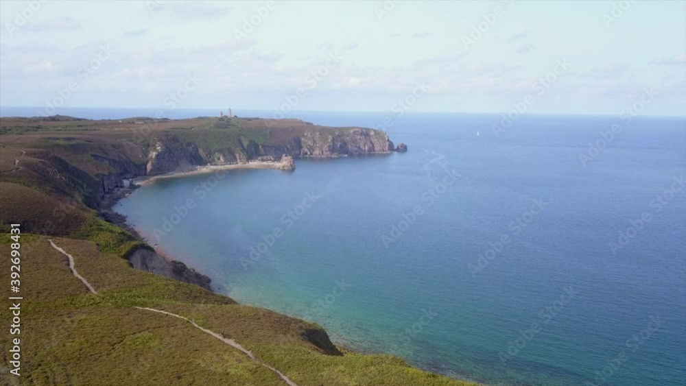 drone flight over coastline with headland of Cap Frehel, Brittany, France, lighthouse, green grass, rocky cliffs, stone beach, blue sea and blue sky drone flight over coastline with headland of Cap Frehel, Brittany, France, lighthouse, green grass, rocky cliffs, stone beach, blue sea and blue sky