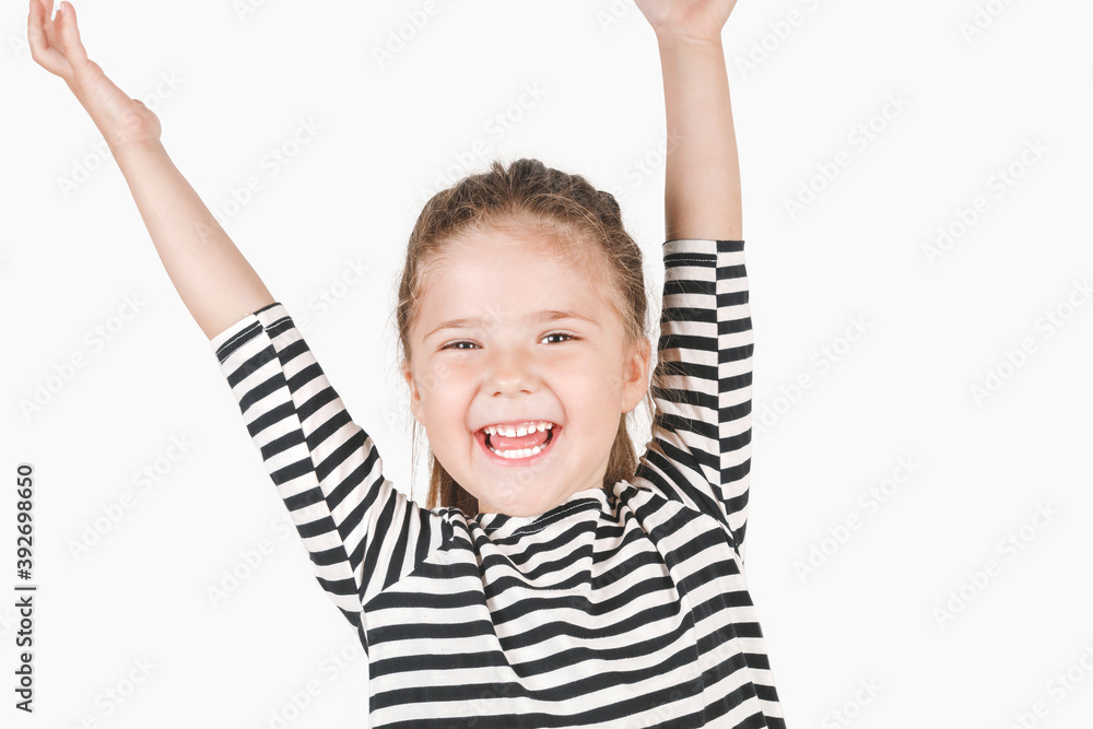 Cute laughing girl looking at camera. Happy girl with wide smile and hands up shouting Surprise, Win. Posing little girl wearing striped shirt. Celebrating concept. Cute laughing girl looking at camera. Happy girl with wide smile and hands up shouting Surprise, Win. Posing little girl wearing striped shirt. Celebrating concept.
