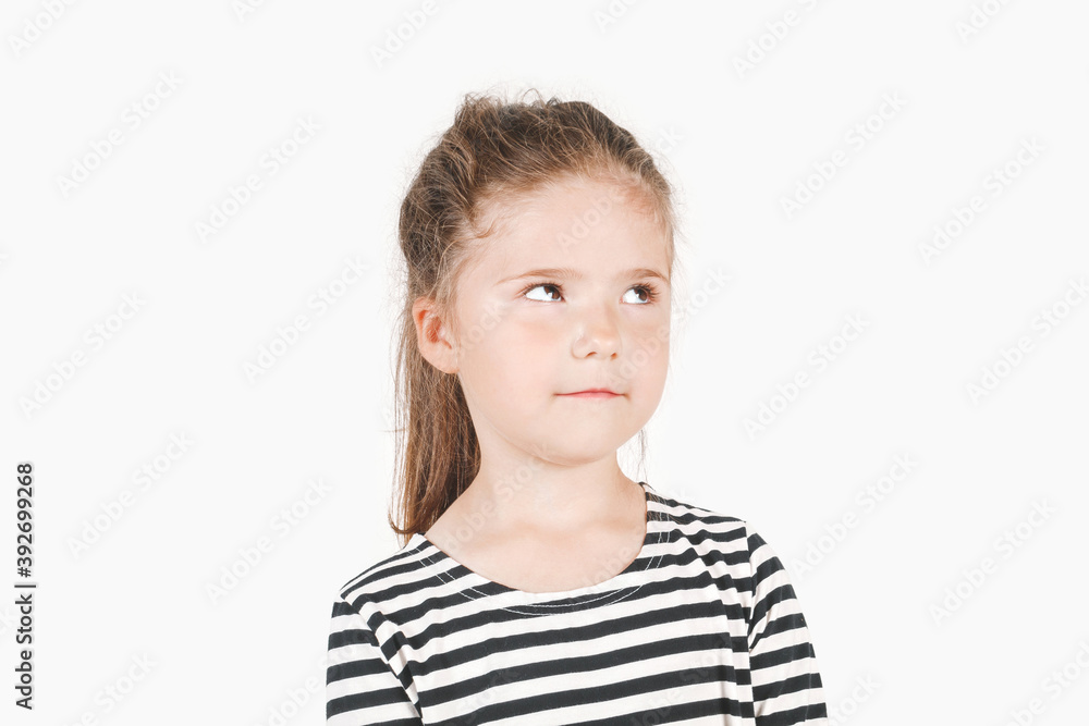 Thinking girl looking up aside. Posing a little girl wearing a striped shirt. Girl is trying to hide something and not to look at camera. Isolated background. Secret, mystery concept. Thinking girl looking up aside. Posing a little girl wearing a striped shirt. Girl is trying to hide something and not to look at camera. Isolated background. Secret, mystery concept.