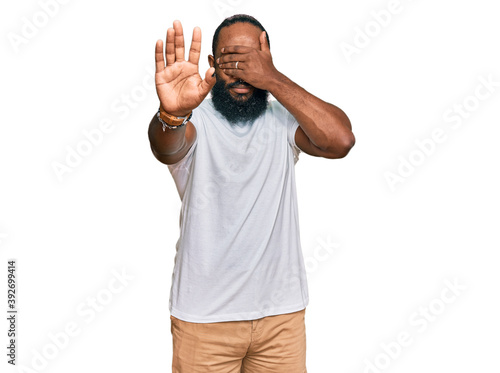 Young african american man wearing casual white tshirt covering eyes with hands and doing stop gesture with sad and fear expression. embarrassed and negative concept.