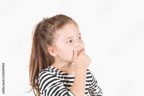 Thoughtful girl looking seriously aside and touching her chin with hand. Pensive thinking girl with eyes directed sideways on copy space. Posing little girl wearing striped shirt.
