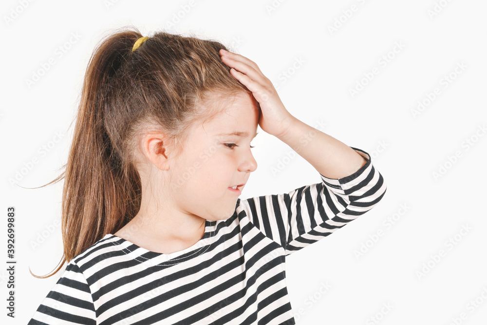 Facepalm. Upset girl looking down aside, holding hand on forehead. Forgetful girl expressing sorrow, blaming herself for bad memory. Posing a little girl wearing a striped shirt. Isolated background. Facepalm. Upset girl looking down aside, holding hand on forehead. Forgetful girl expressing sorrow, blaming herself for bad memory. Posing a little girl wearing a striped shirt. Isolated background.