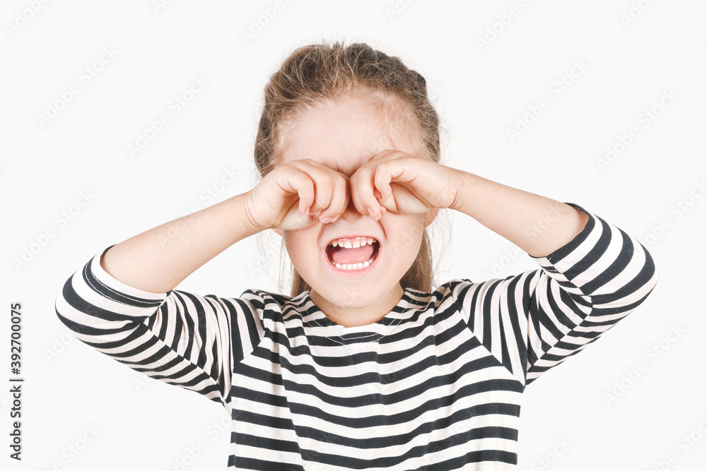 Loudly crying girl with hands covering her eyes. The upset girl is wiping tears with two hands. Posing little girl wearing a striped shirt. Negative emotion, depression, stress concept. Loudly crying girl with hands covering her eyes. The upset girl is wiping tears with two hands. Posing little girl wearing a striped shirt. Negative emotion, depression, stress concept.