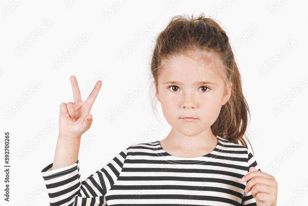 Serious girl with two fingers up, showing Number two and peace or victory symbol. Close up of posing little girl wearing a striped shirt, looking at the camera on an isolated background. Serious girl with two fingers up, showing Number two and peace or victory symbol. Close up of posing little girl wearing a striped shirt, looking at the camera on an isolated background.