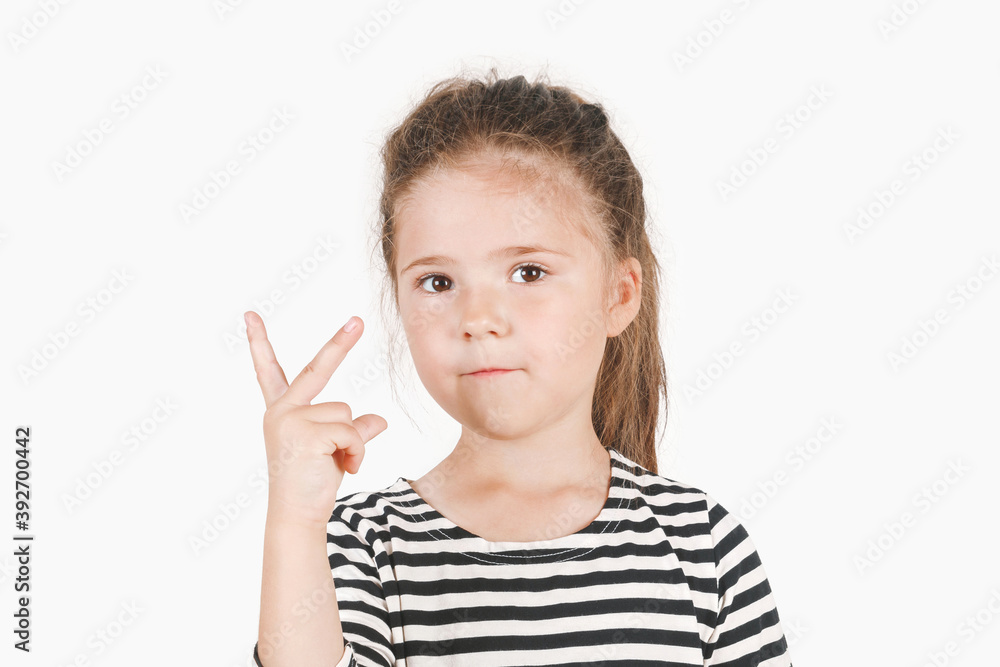 Serious girl with two fingers up, showing Number two and peace or victory symbol. Close up of posing little girl wearing a striped shirt, looking at the camera on an isolated background. Serious girl with two fingers up, showing Number two and peace or victory symbol. Close up of posing little girl wearing a striped shirt, looking at the camera on an isolated background.