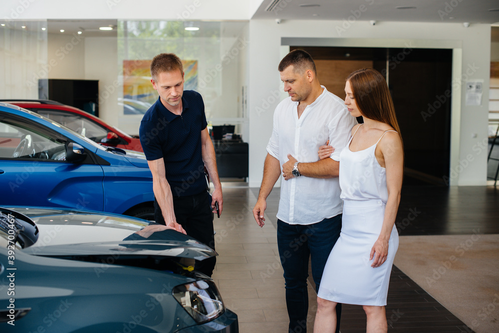 Fototapeta premium A young couple chooses a new car at the dealership and consults with a representative of the dealership. Used cars for sale. Dream fulfillment